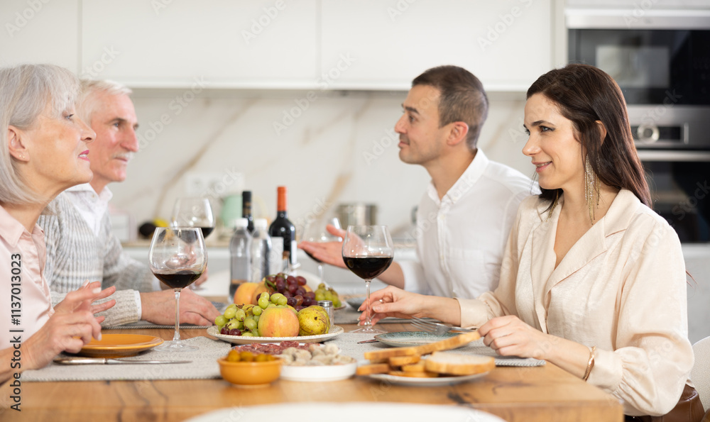 Mature couple are sitting at table with younger spouses friend, drinking wine and enjoying snacks, chatting merrily, raise glass to, celebrating important event. Mature couple are sitting at table with younger spouses friend, drinking wine and enjoying snacks, chatting merrily, raise glass to, celebrating important event.
