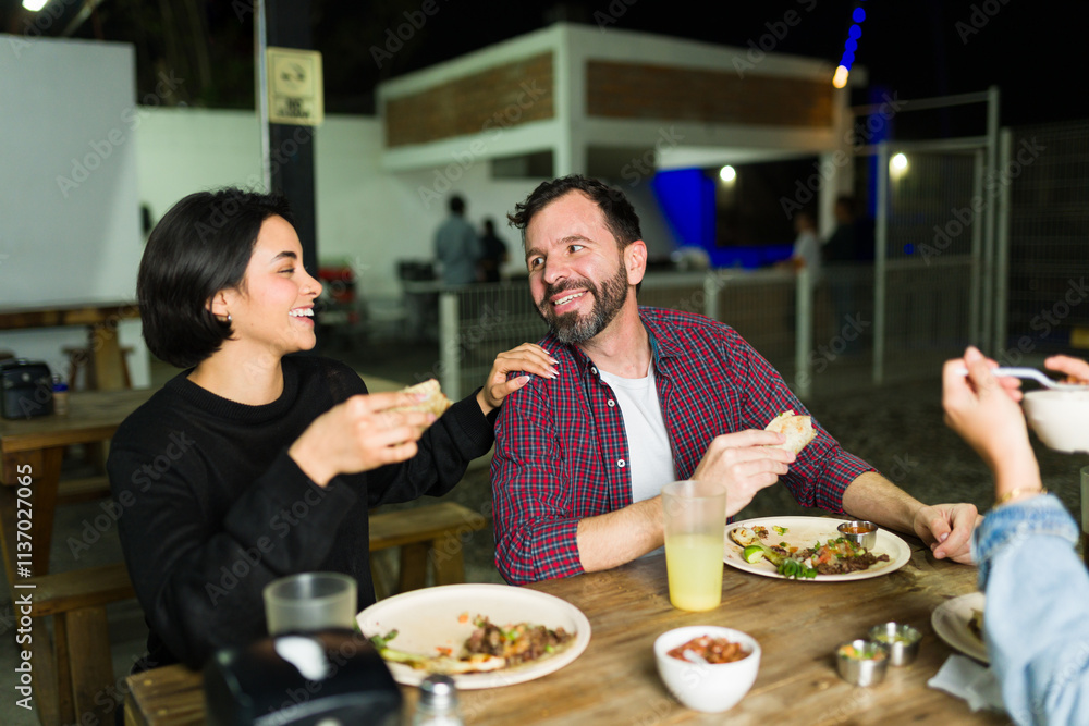 Friends enjoying a meal at an outdoor mexican taqueria, eating tacos and chatting happily Friends enjoying a meal at an outdoor mexican taqueria, eating tacos and chatting happily