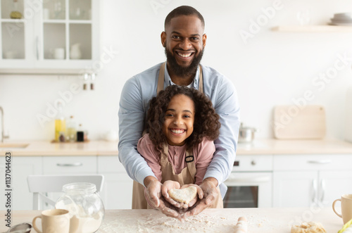 Bonding And Togetherness Concept. Portrait of happy african american dad and daughter baking in the kitchen and holding dough in heart shape in hands, preparing present for mother's day