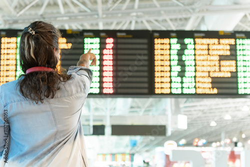 Traveler points at flight information board in bustling airport