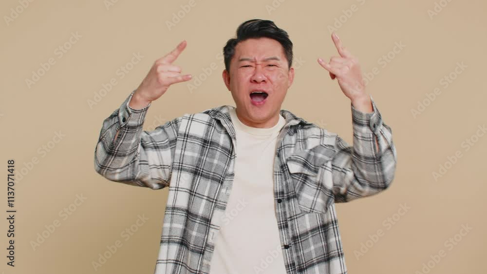 Overjoyed happy Asian middle-aged man showing rock n roll gesture by hands cool sign shouting yeah with crazy expression, dancing, rejoicing victory win success. Mature Chinese guy on beige background Overjoyed happy Asian middle-aged man showing rock n roll gesture by hands cool sign shouting yeah with crazy expression, dancing, rejoicing victory win success. Mature Chinese guy on beige background