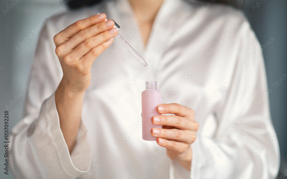 In a modern bathroom, a young Caucasian woman with brunette hair enjoys a skincare routine. She carefully uses a dropper to apply a gentle serum, embracing self-care and relaxation. In a modern bathroom, a young Caucasian woman with brunette hair enjoys a skincare routine. She carefully uses a dropper to apply a gentle serum, embracing self-care and relaxation.