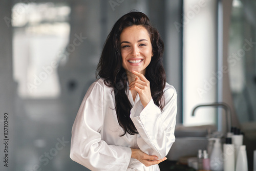 In a cozy bathroom, a young Caucasian woman smiles while pampering herself. She is enjoying a skincare routine, radiating beauty and confidence in her relaxing space.