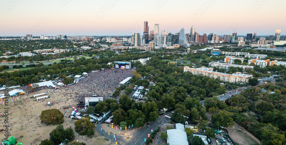 Naklejka premium Aerial view of a large outdoor music festival in a vibrant Austin, Texas at sunset with Lady Bird Lake