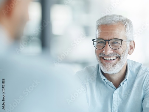 A smiling elderly man with glasses shares a joyful moment in a bright, modern setting, embodying happiness and wisdom.