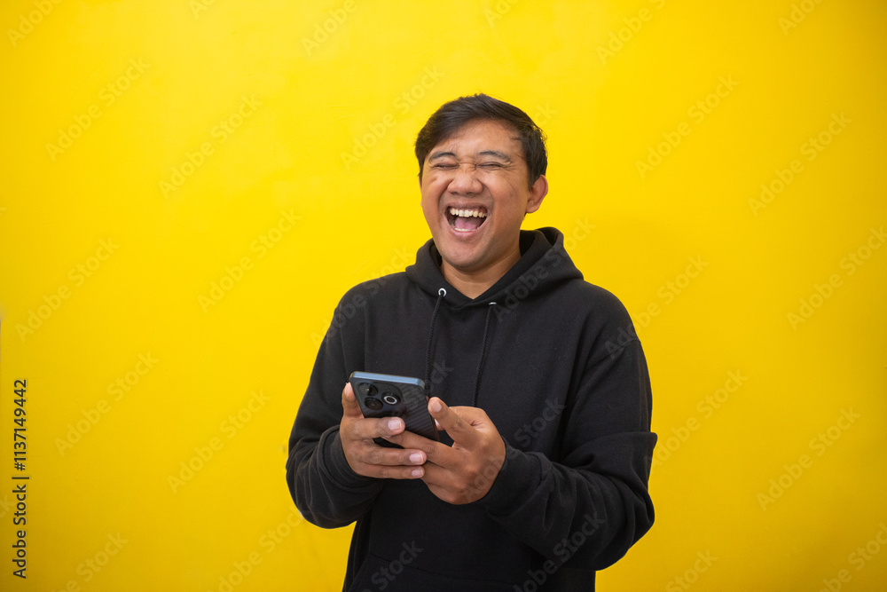Smiling Asian man (Indonesian) hold phone isolated yellow background. Smiling Asian man (Indonesian) hold phone isolated yellow background.