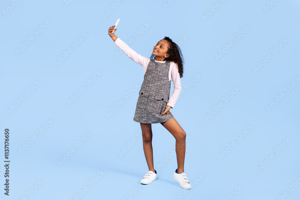 A joyful girl stands confidently while taking a selfie. Her cheerful expression and playful pose embody the spirit of childhood and fun. The vibrant blue background emphasizes her happiness. A joyful girl stands confidently while taking a selfie. Her cheerful expression and playful pose embody the spirit of childhood and fun. The vibrant blue background emphasizes her happiness.