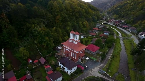 A view of the village of Valea Ierii nestled in a valley, Cluj, Transylvania, Romania, with colorful autumn trees, a river flowing through, and a beautiful church as the centerpiece. photo