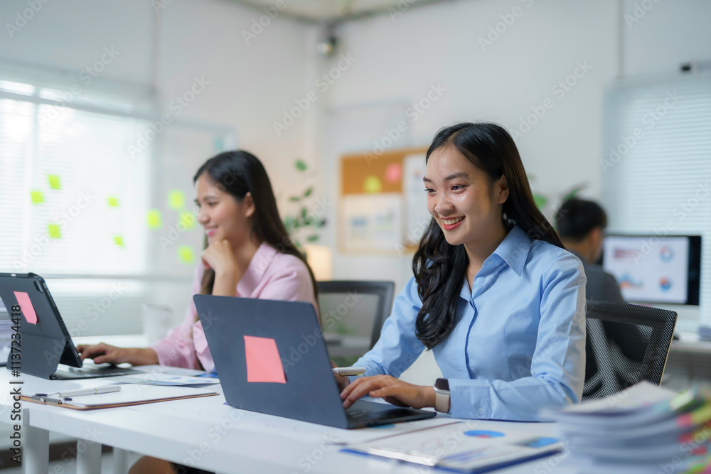 Young asian businesswoman smiling and working with laptop computer at office desk with colleagues Young asian businesswoman smiling and working with laptop computer at office desk with colleagues