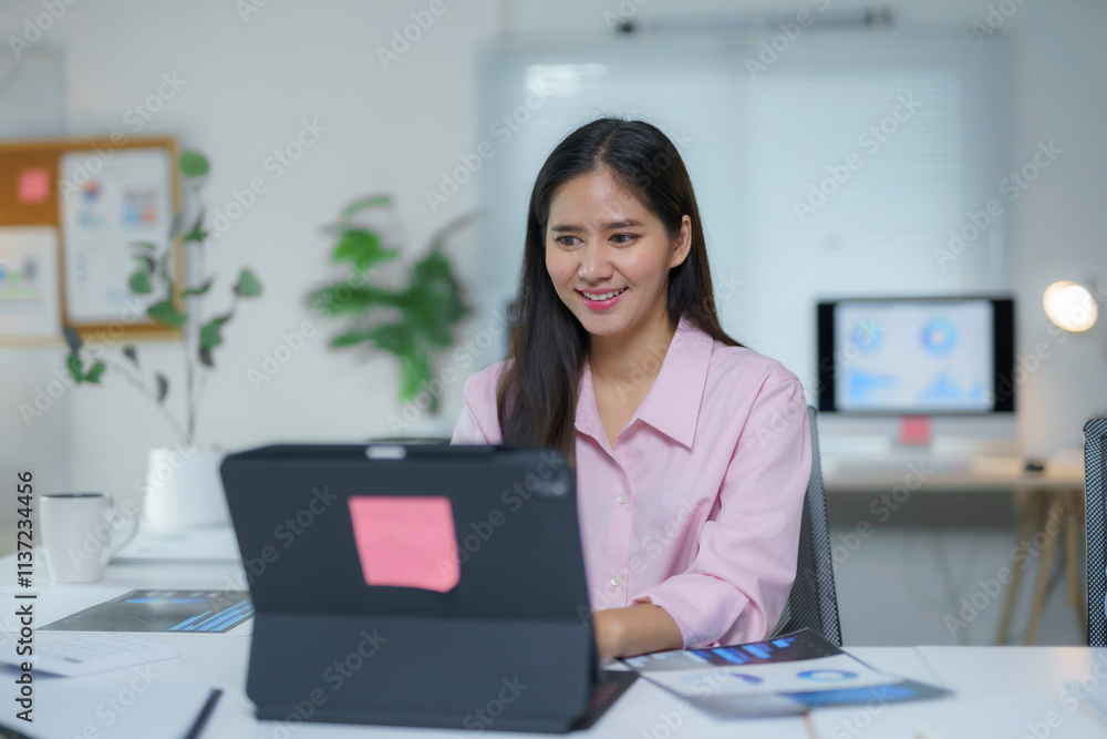 Young asian businesswoman smiling and working on tablet with charts and graphs in modern office Young asian businesswoman smiling and working on tablet with charts and graphs in modern office