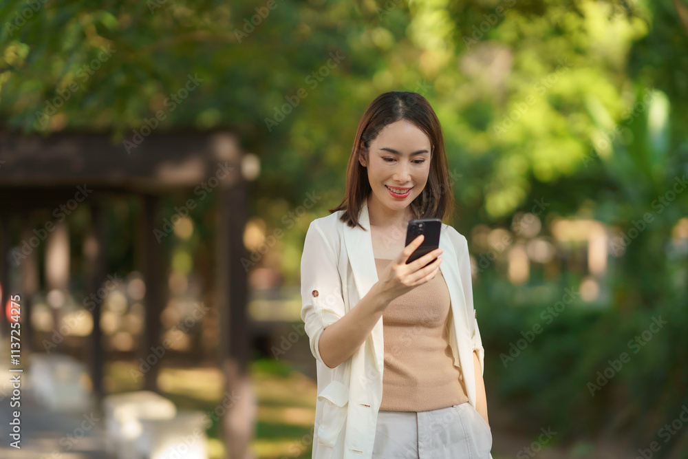 Businesswoman smiling and enjoying her smartphone in a lush green park, embracing the tranquility of nature on a sunny day Businesswoman smiling and enjoying her smartphone in a lush green park, embracing the tranquility of nature on a sunny day