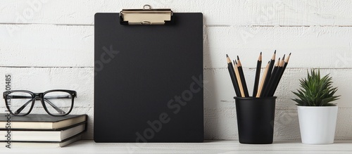 Simple desk setup with A4 paper, glasses, books, and pencil cup next to clipboard.