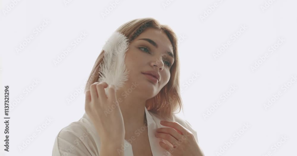 Portrait of young beautiful woman with nude makeup holding playing with feather on face. Beautiful Young Woman with Clean Fresh Skin. Skin care concept at home. Portrait of young beautiful woman with nude makeup holding playing with feather on face. Beautiful Young Woman with Clean Fresh Skin. Skin care concept at home.