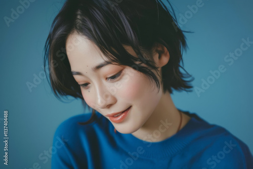 Portrait photo of a Asian female model looking down at something with a smiling face isolated on a blue background photo