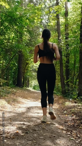 Young beautiful fitness woman in black top and leggings running outdoor in park at warm summer day. Female athlete jogging in the forest. Tracking cinematic slow motion shot. Fitness workout