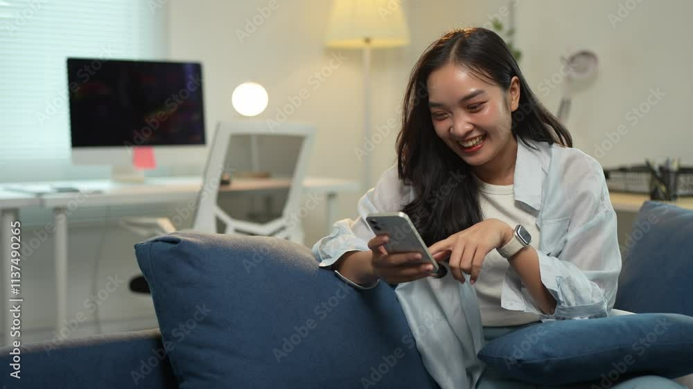 Attractive Asian woman holding mobile phone for online shopping, e-commerce, online shopping, texting, greeting, chatting, reading book, relaxing, hobby and relaxing on sofa in living room at home.