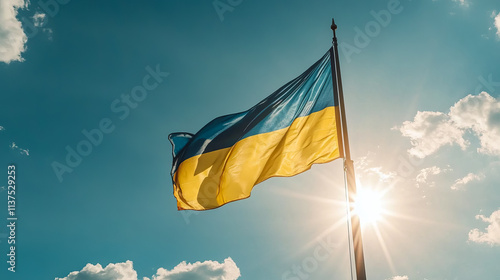 A vibrant Ukrainian flag waves proudly on a flagpole against a bright blue sky and shining sun. photo