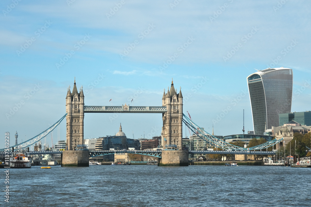 Obraz premium Iconic Tower Bridge in London over the River Thames with the city skyline, including modern skyscrapers like the Walkie Talkie building, under a clear blue sky. Historic architecture meets modernity