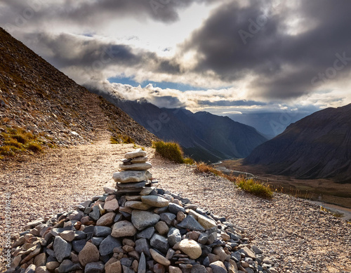 A pile of gravel, sand, and stones stacked beside a rocky mountain trail under cloudy skies photo