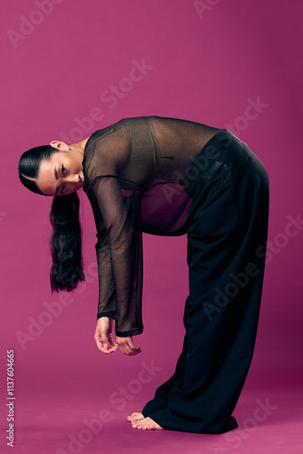 Fashion asian woman in sheer top bending over with hands on knees, head tilted on purple background photo