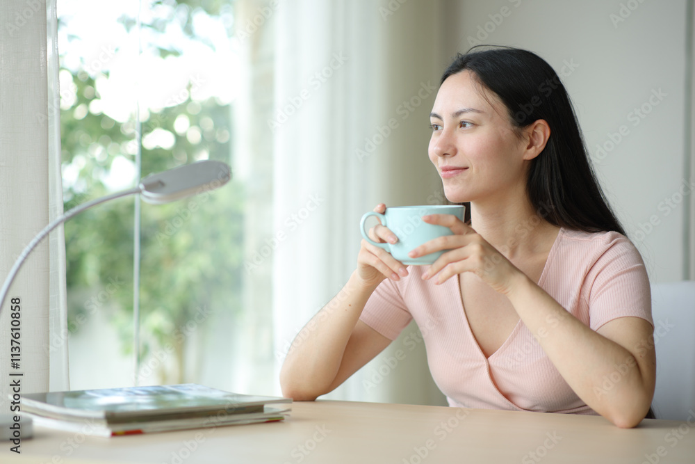 Asian woman looking though a window drinking at home Asian woman looking though a window drinking at home