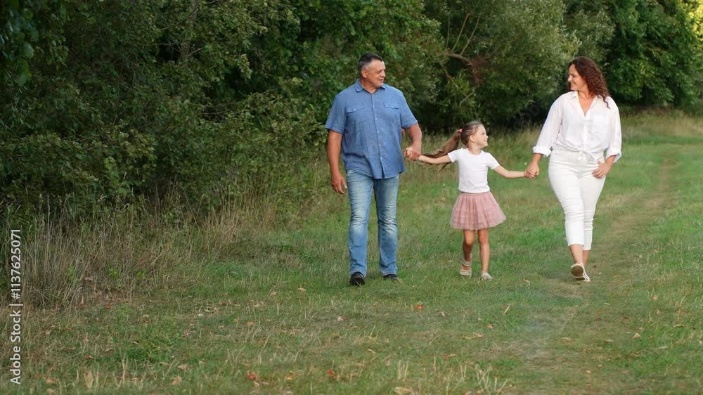 Happy family walking together in park on summer day. Mom, dad, daughter have fun together outdoors, walking on path and grass. Happy family, love and parenthood concept. International Day of Families Happy family walking together in park on summer day. Mom, dad, daughter have fun together outdoors, walking on path and grass. Happy family, love and parenthood concept. International Day of Families
