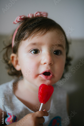 Cute baby girl eating a heart shaped lollipop at home photo