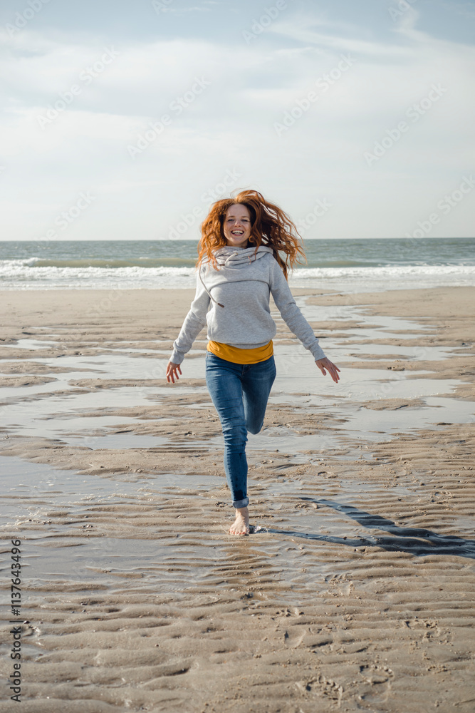 Netherlands, Zeeland, happy redheaded woman running on the beach Netherlands, Zeeland, happy redheaded woman running on the beach
