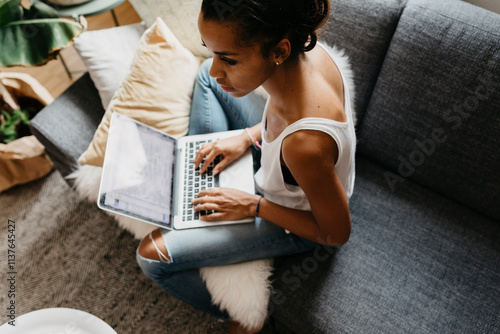 Young woman sitting on the couch at home using laptop photo