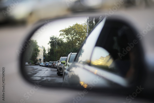 Billede på lærred Rearview Mirror Perspective of Urban Street with Parked Cars and Trees