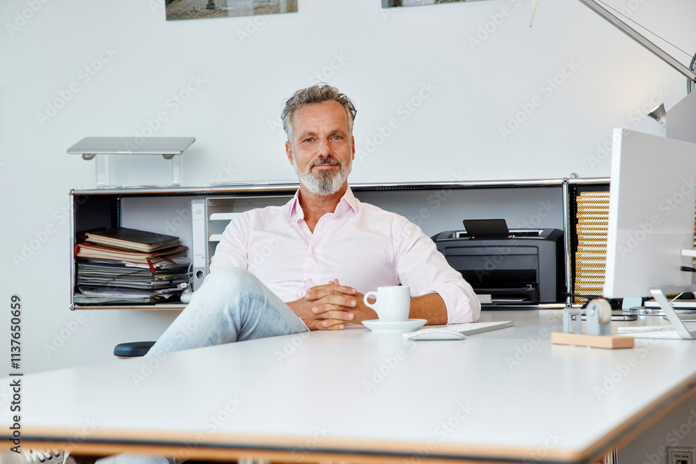 © Westend61 - Portrait of confident businessman sitting at desk in office © Westend61 - Portrait of confident businessman sitting at desk in office