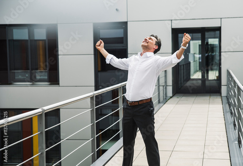 Cheering businessman standing on skywalk at office building photo