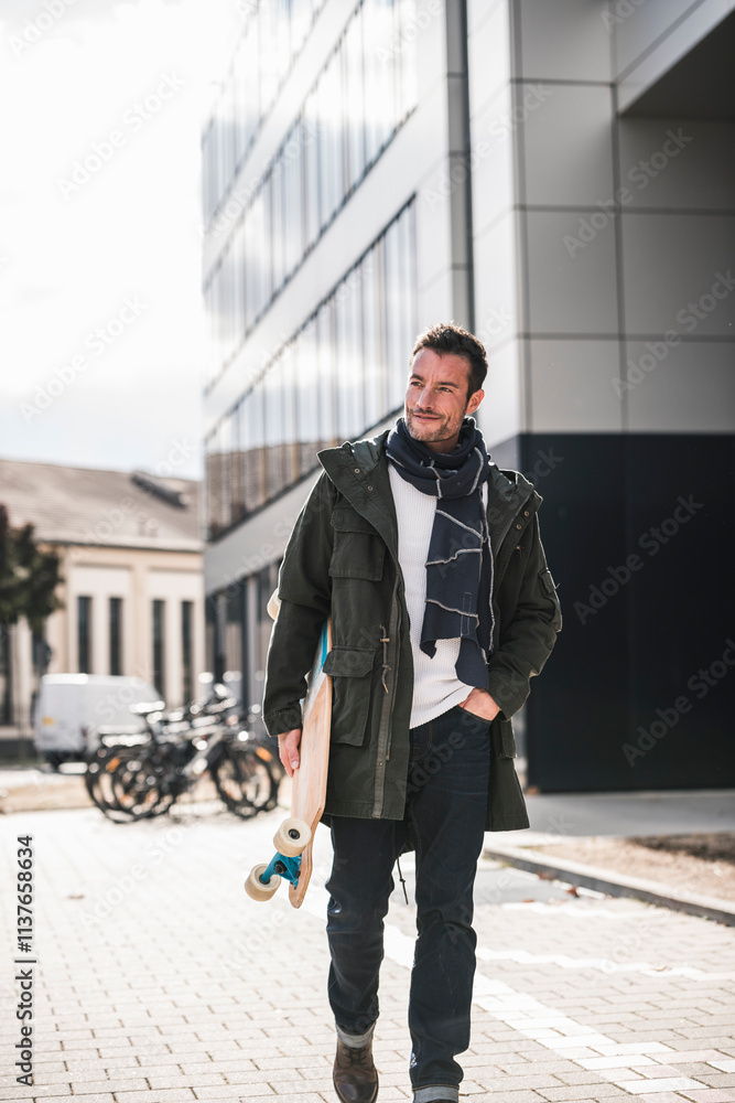 Mature man, wearing coat and scarf, walking in the city, carrying longboard