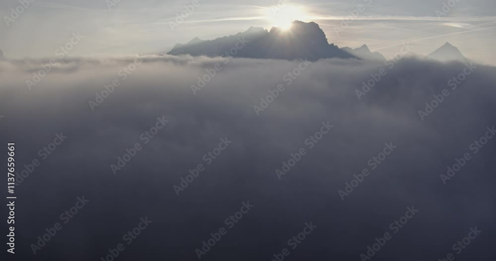 Flying above the clouds, with sun rising behind a mountain peak, atmospheric mood Flying above the clouds, with sun rising behind a mountain peak, atmospheric mood