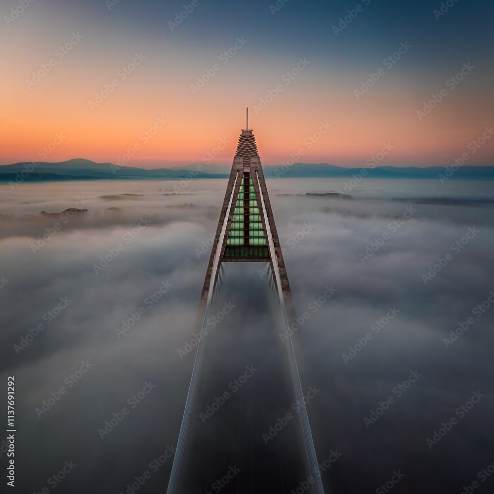 Budapest, Hungary - Aerial view of one of the pillars of the Megyeri Bridge over River Danube covered in heavy autumn fog at sunset with blue and golden sky