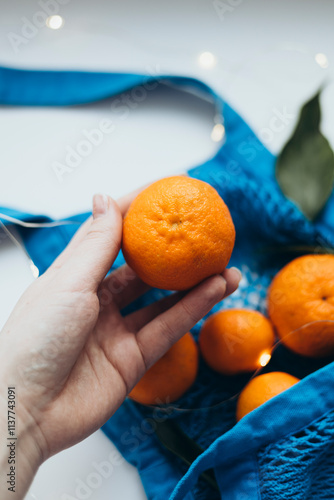 Cropped image of a hand holding a tangerine over a string bag photo