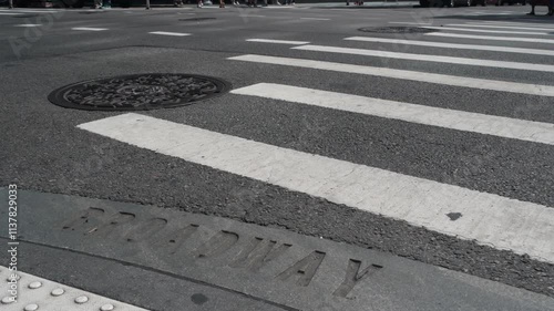 Broadway street sign, people on pedestrian zebra crossroad. New York City Manhattan road intersection. Text on asphalt near crosswalk, shadows on crossroad ped crossing. Traffic signage, United States