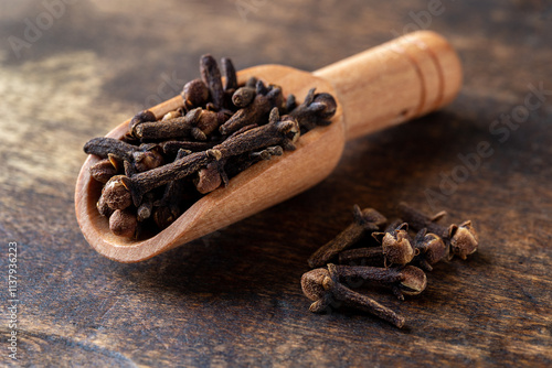 Dry clove buds in a wooden scoop macro. Scoop full of whole cloves spice over wooden surface. Spice for cooking and herbal medicine concept. photo