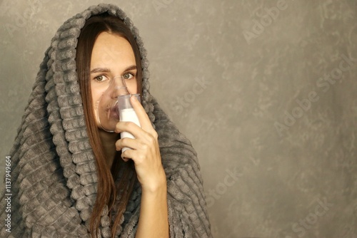 A young woman with a portable inhaler.Portrait of a young woman doing inhalation at home. Use nebulizer and inhaler for the treatment.