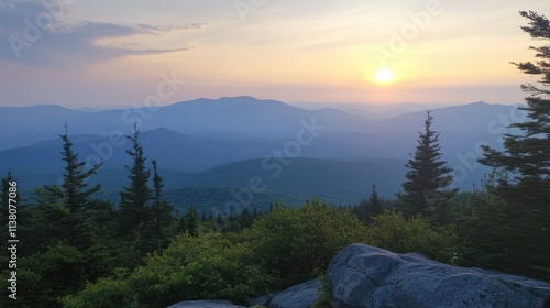 Serene sunset view from a mountain peak surrounded by lush trees and rolling hills in the distance with soft pastel skies. photo