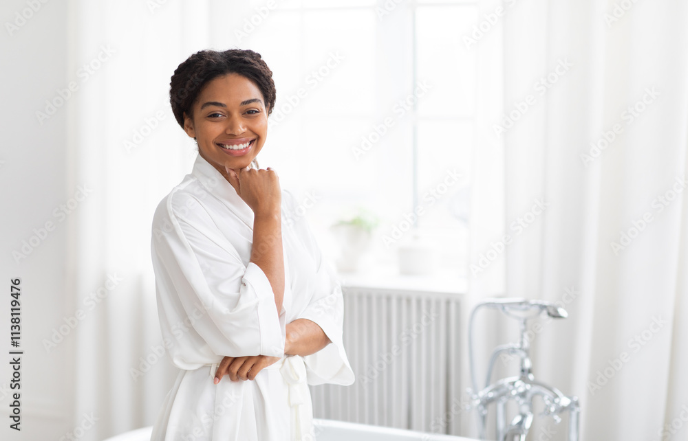 A cheerful African American woman stands in her home bathroom, wearing a cozy white robe. She smiles while pampering herself, showcasing her love for skincare in a bright, fresh space. A cheerful African American woman stands in her home bathroom, wearing a cozy white robe. She smiles while pampering herself, showcasing her love for skincare in a bright, fresh space.