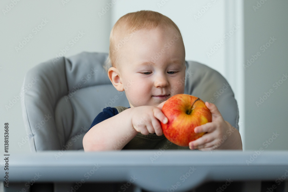 Smiling baby sitting at baby table and holding big ripe apple. Closeup. Smiling baby sitting at baby table and holding big ripe apple. Closeup.