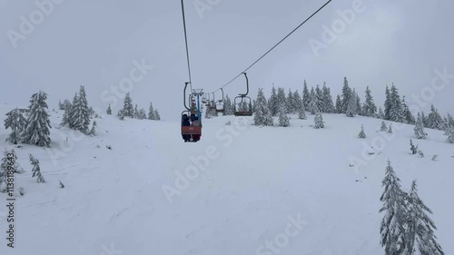 Skier and snowboarder on ski lift in snowy forest close-up