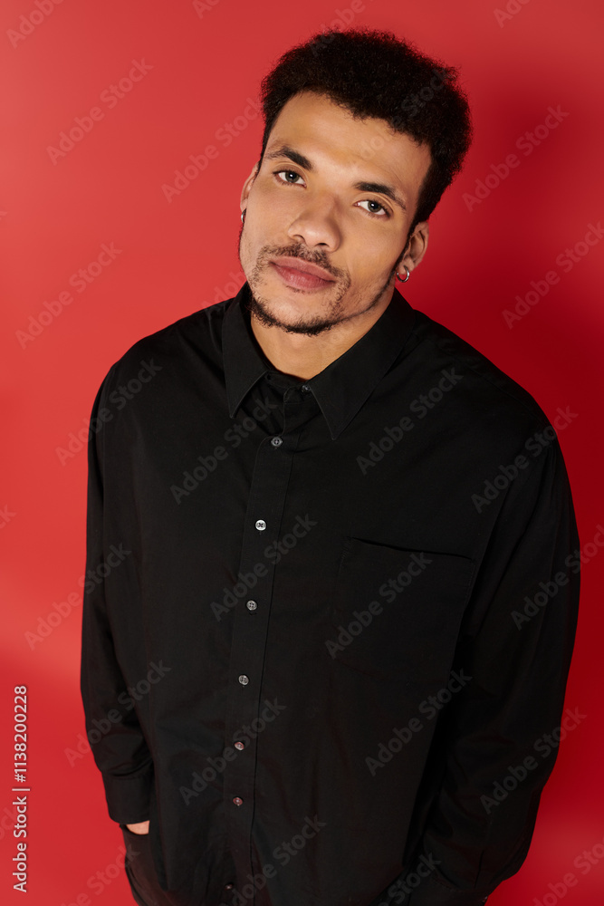 A young, handsome man in a stylish black shirt stands relaxed against vibrant red. A young, handsome man in a stylish black shirt stands relaxed against vibrant red.