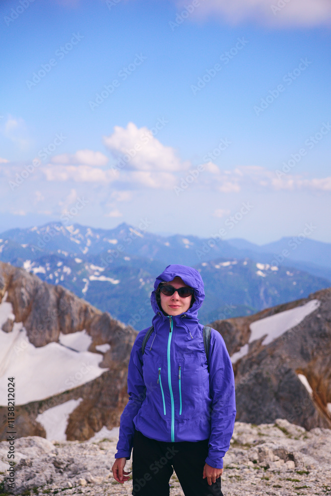 A young girl in sunglasses smiles and looks at the camera against the background of snowy mountain peaks. Mountain trekking and mountaineering in summer A young girl in sunglasses smiles and looks at the camera against the background of snowy mountain peaks. Mountain trekking and mountaineering in summer