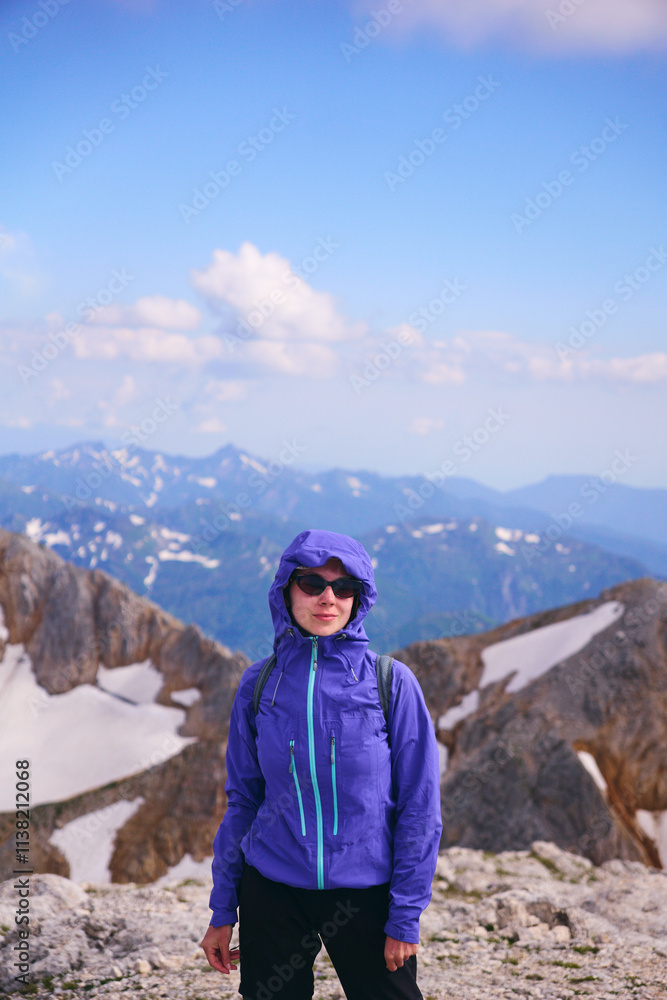 A young girl in sunglasses smiles and looks at the camera against the background of snowy mountain peaks. Mountain trekking and mountaineering in summer A young girl in sunglasses smiles and looks at the camera against the background of snowy mountain peaks. Mountain trekking and mountaineering in summer