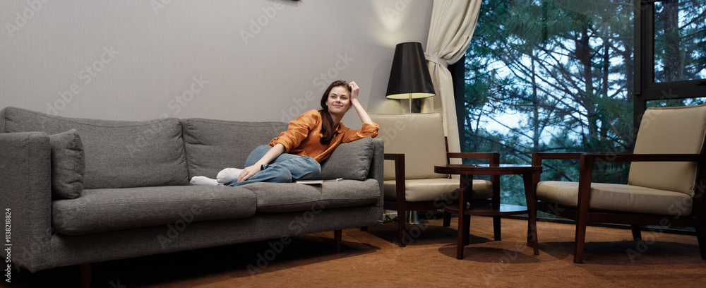 Relaxed woman in casual orange sweater lounging on a cozy sofa, featuring serene window view and modern interior design Relaxed woman in casual orange sweater lounging on a cozy sofa, featuring serene window view and modern interior design