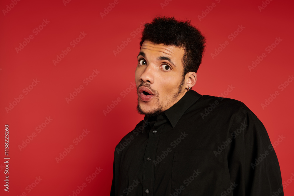 Obraz premium Handsome young man posing with a playful expression in front of a bright red backdrop.