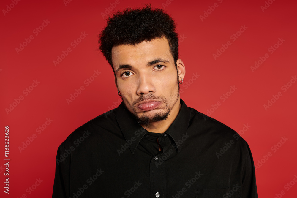 A young handsome man stands in front of a bright red background with a serious expression. A young handsome man stands in front of a bright red background with a serious expression.