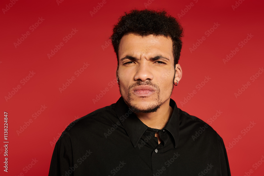 A young man with stylish hair and a serious expression stands against a bright red background. A young man with stylish hair and a serious expression stands against a bright red background.